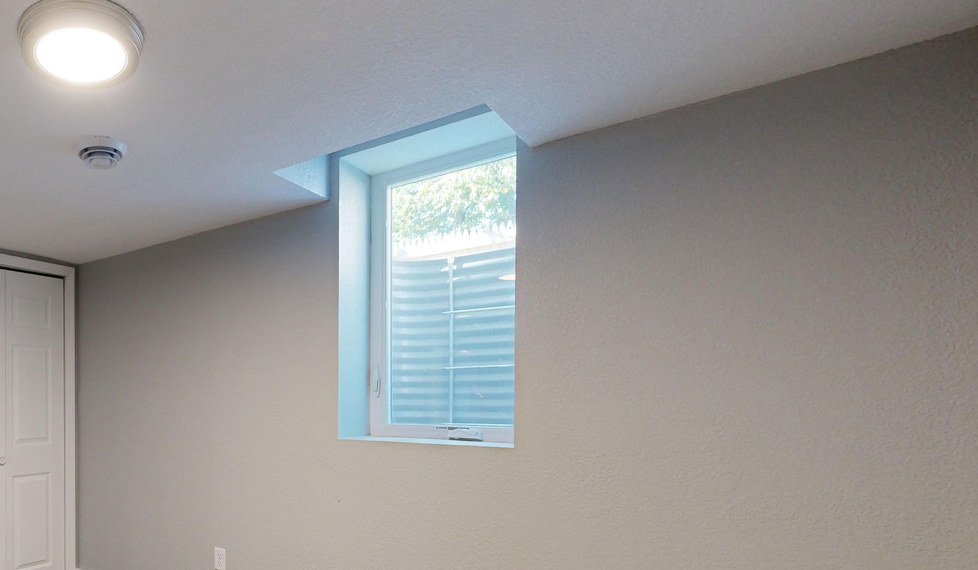 A basement bedroom egress window with the steel window well and escape ladder visible outside